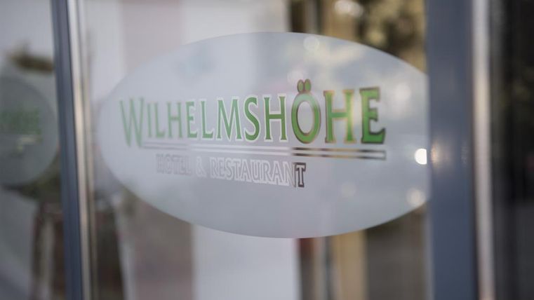 Een transparant bord met de tekst „WILHELMSHÖHE“. Het toont aan dat het om een restaurant gaat.