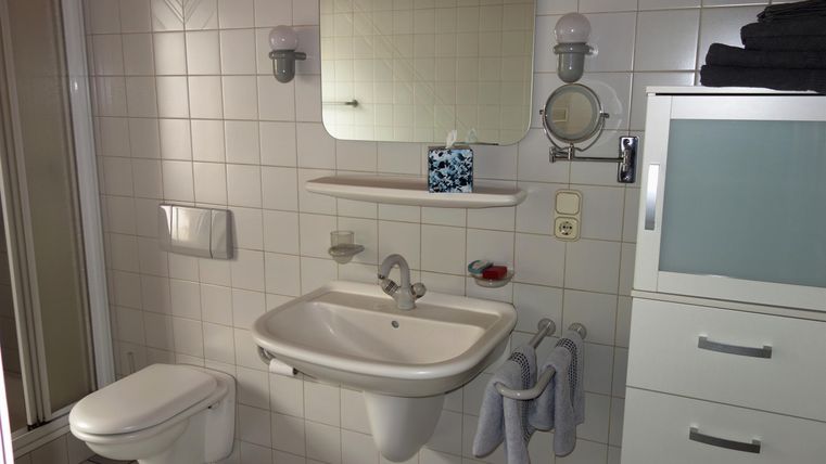 Een moderne badkamer met witte tegels en een wastafel. Op de achtergrond zijn douche en spiegel te zien.
