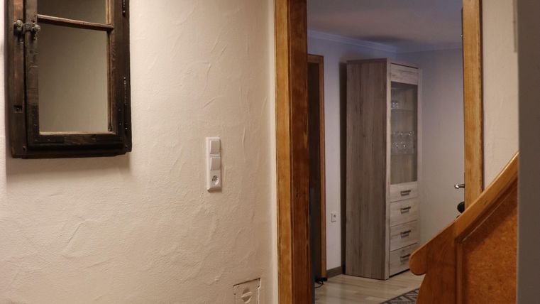 Ein heller Flur mit einer gemütlichen Sitzgelegenheit und einem Spiegel. Im Hintergrund sieht man eine offene Tür, die zu einem weiteren Raum führt.