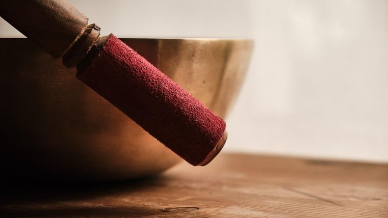 Een metalen klankschaal staat op de voorgrond. De hamer met rode vilt is gereed om bespeeld te worden.