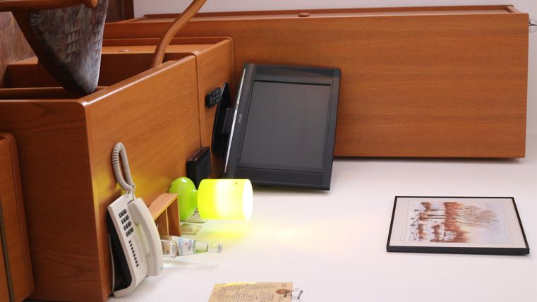 Ein Arbeitsbereich mit Holzmöbeln, einem Computer und verschiedenen Bürogegenständen. Es gibt ein Foto und eine Lampe auf dem Tisch.