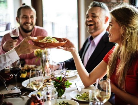 Group of people in a restaurant, laughing and sharing food together. They enjoy wine and pasta in a sociable atmosphere.