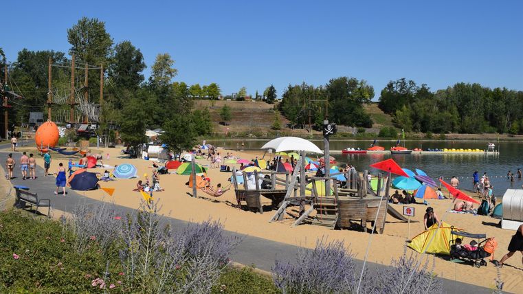 Ein belebter Strand mit vielen Sonnenliegen und Sonnenschirmen. Menschen genießen den Tag am Wasser unter klarem Himmel.