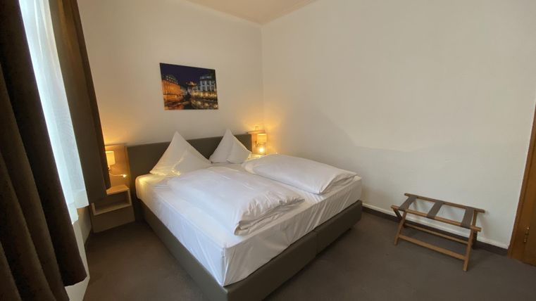 Ein gemütliches Schlafzimmer mit zwei Einzelbetten und warmem Licht. An der Wand hängt ein Bild, und es gibt einen kleinen Hocker für zusätzlichen Komfort.