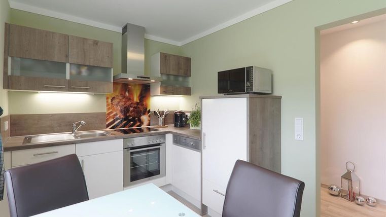 Een moderne keuken met houten kasten en roestvrijstalen apparaten. De ruimte is licht en vriendelijk met een grote tafel en stoelen.