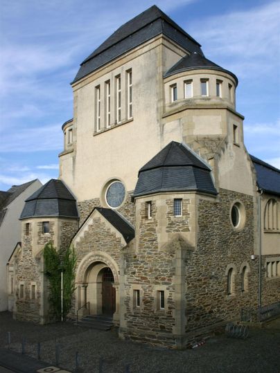Eine historische Kirche mit einer beeindruckenden Fassade aus Stein und einem modernen Dach. Der Bau ist von einer malerischen Umgebung umgeben.