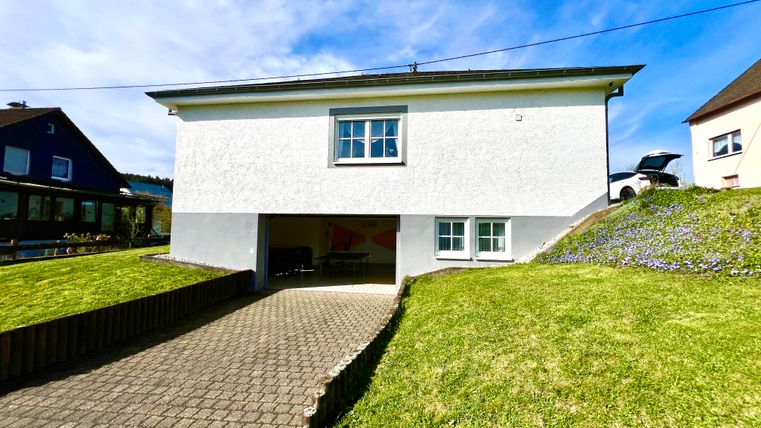 A modern two-story house with a white facade and a garage area. The well-maintained garden and the blue sky create a friendly atmosphere.