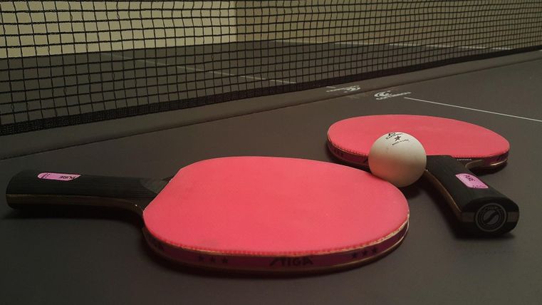Two table tennis rackets with red hitting surfaces and a ball lie on a dark table tennis table.