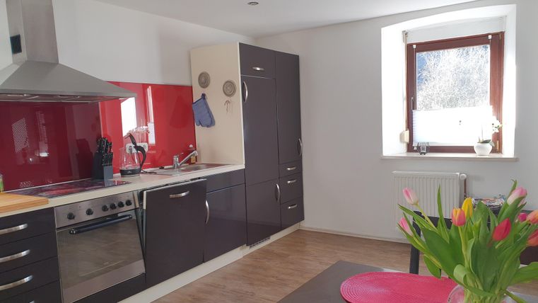 Een moderne keuken met rode en zwarte kasten. Er is een eettafel met verse bloemen en veel natuurlijk licht.