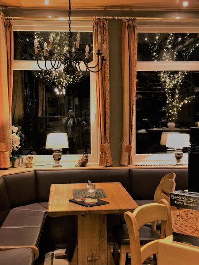 Ein gemütlicher Innenraum mit einem Holztisch und einer Bank. Die Fenster sind geschmückt mit warmem Licht und eleganten Vorhängen.